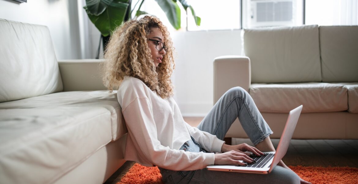 woman sitting on floor and leaning on couch using laptop